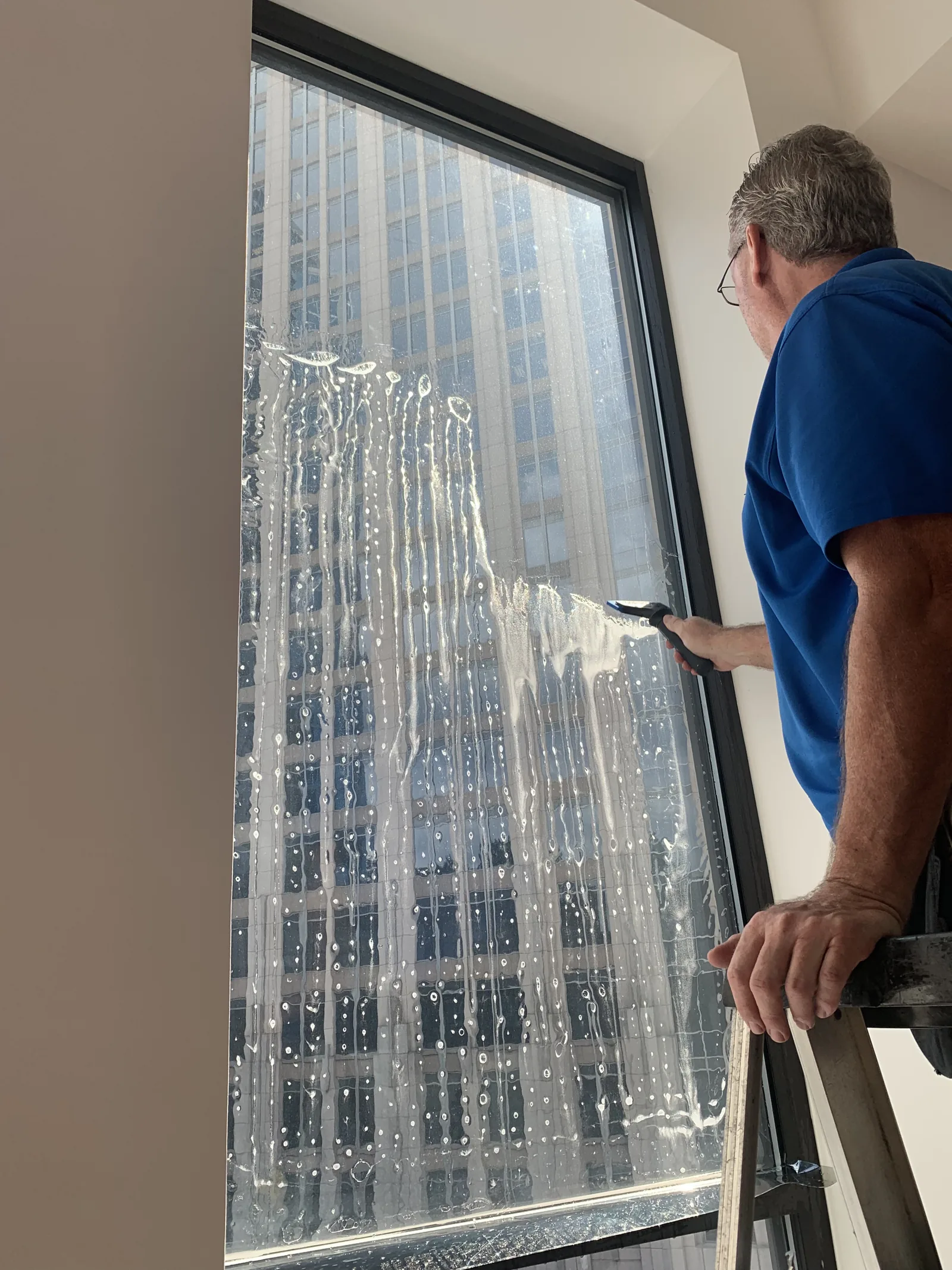 Hand-cleaning a high window with a city skyline reflection in Charlotte