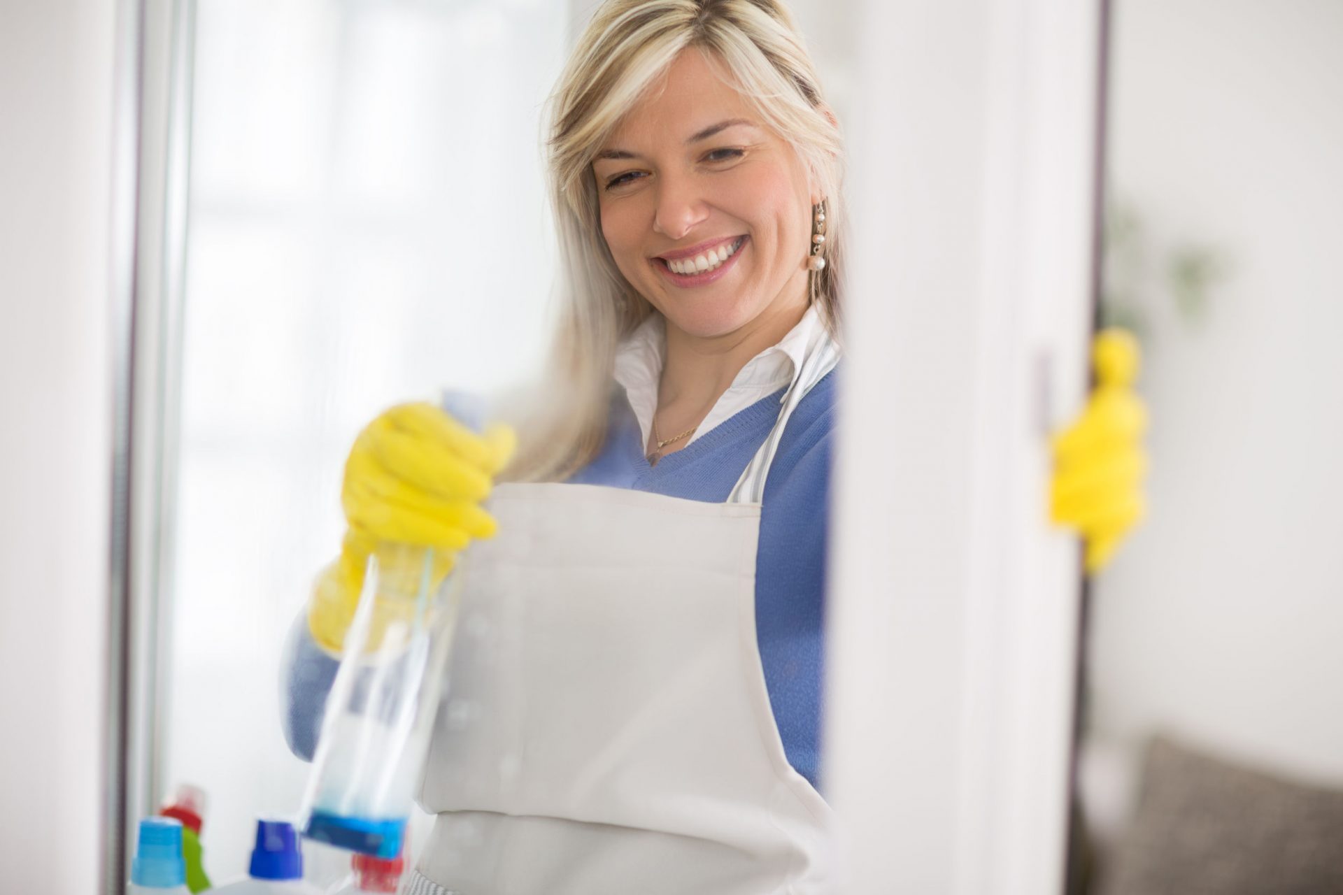 Woman wearing apron sprays window cleaning product on glass